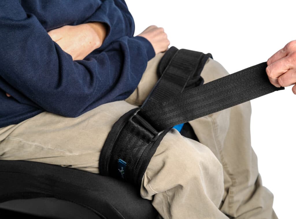 A wheelchair users legs are being shown sat in wheelchair with a leg strap securing the thighs of the legs together