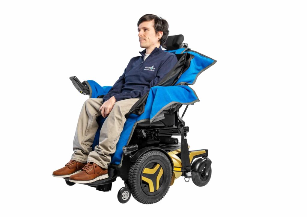 Josh Wintersgill sat in his powered wheelchair with an ableSling Lite (a transfer sling) whilst sat on an ableDry (wheelchair cover to keep the seating area dry).