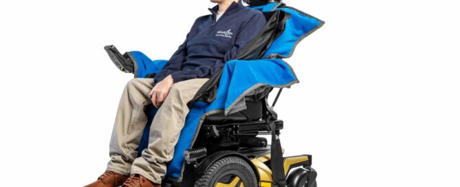 Josh Wintersgill sat in his powered wheelchair with an ableSling Lite (a transfer sling) whilst sat on an ableDry (wheelchair cover to keep the seating area dry).